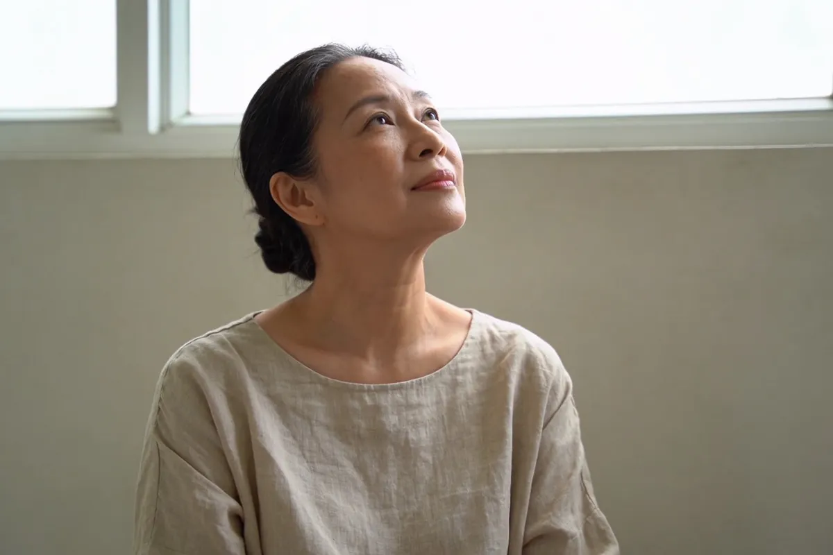 A woman in her forties lifting her chin toward soft window light (illustrative image, not a patient)