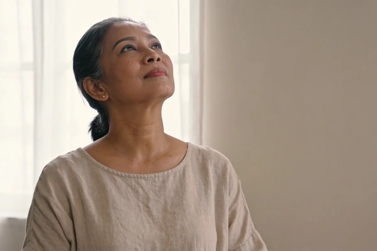 A woman in her forties lifting her chin toward soft window light (illustrative image, not a patient)