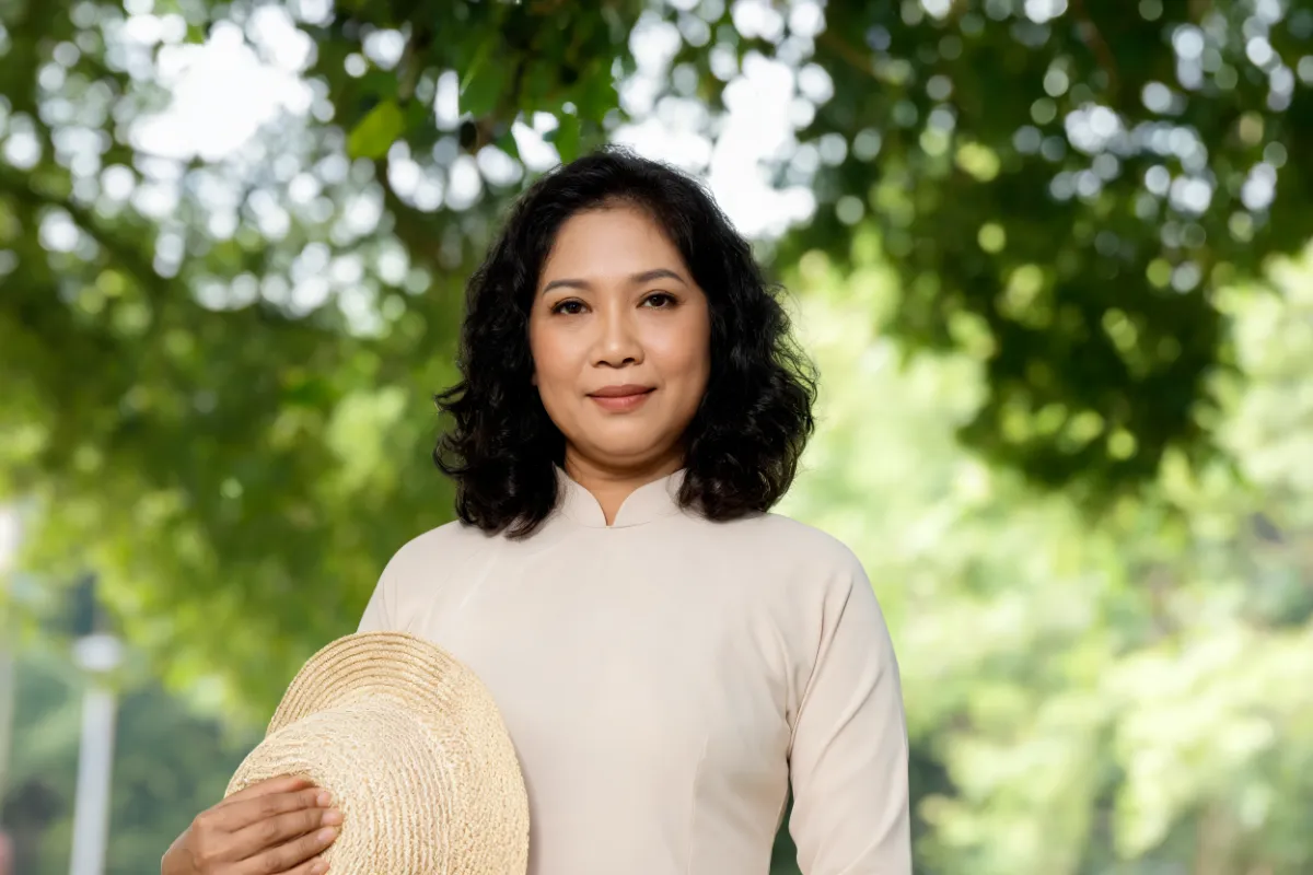 A woman in her forties holding a sun hat in outdoor shade (illustrative image, not a patient)
