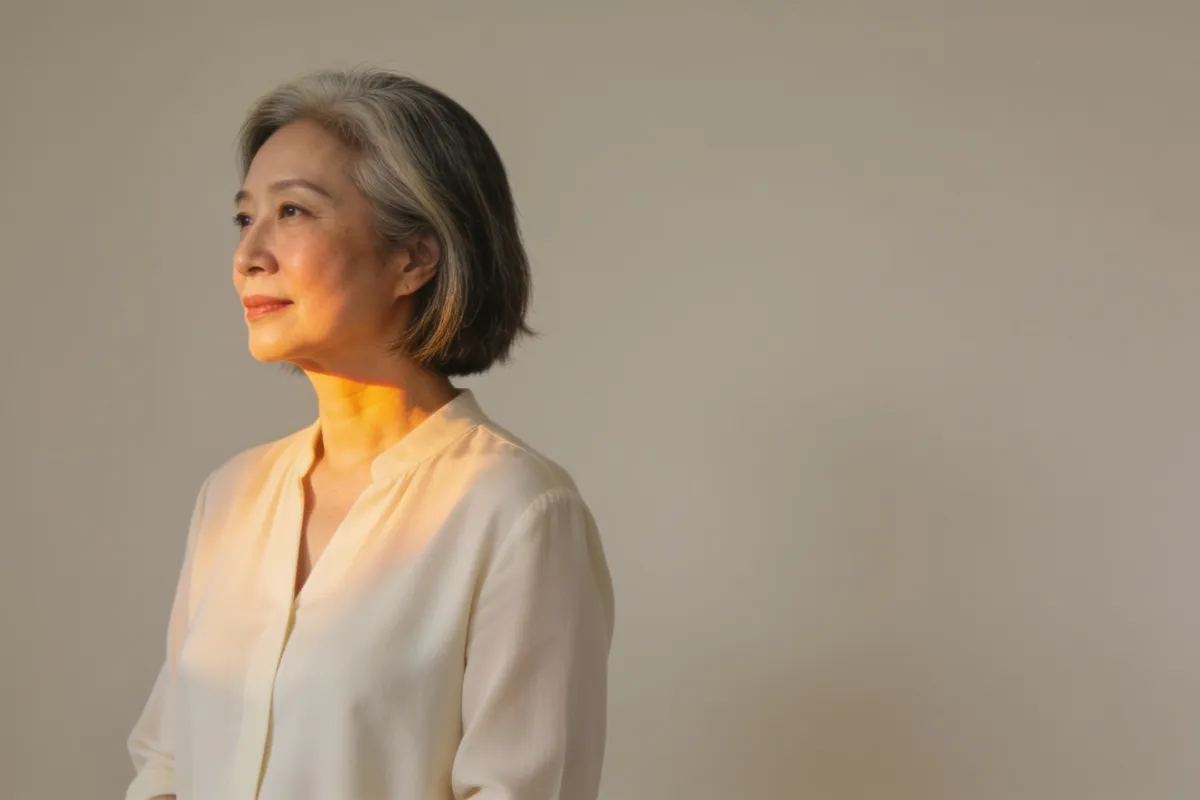 A woman in her fifties with a grey-streaked bob, face turned toward warm side light (illustrative image, not a patient)